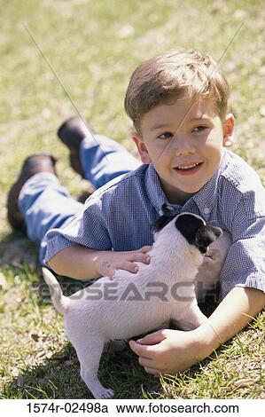 Stock Image - Boy lying on a lawn holding a puppy. Fotosearch