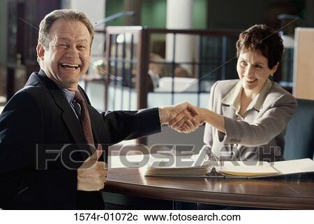 Stock Image - Businesswoman and a businessman shaking hands. Fotosearch