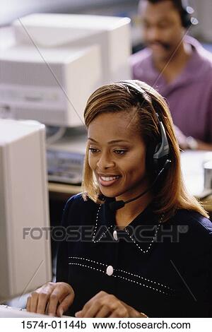 Stock Image - Businesswoman wearing a headset working on a computer. Fotosearch