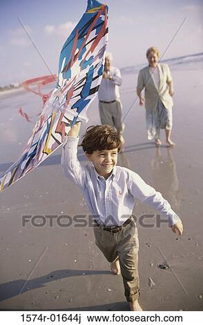 Stock Image - Child flying a kite at the beach with his grandparents. Fotosearch
