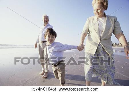 Stock Image - Child walking on the beach with his grandparent. Fotosearch