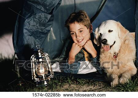 Stock Image - Close-up of a boy camping in a tent with his dog. Fotosearch