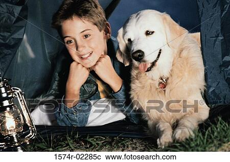 Stock Image - Close-up of a boy camping in a tent with his dog. Fotosearch