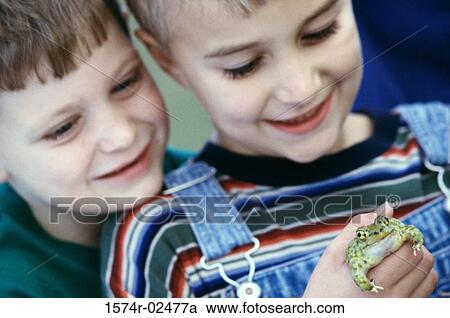 Stock Image - Close-up of a boy standing with his friend holding a frog. Fotosearch