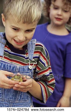 Close-up of a boy standing with his friend holding a frog View Large Photo Image Stock Image - Close-up of a boy standing with his friend holding a frog. Fotosearch