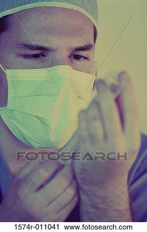 Stock Image - Close-up of a male doctor wearing scrubs holding out a syringe. Fotosearch
