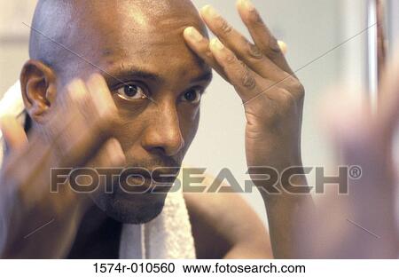 Stock Image - Close-up of a young man examining his forehead. Fotosearch