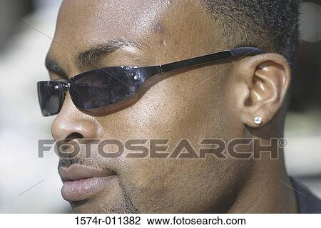 Stock Image - Close-up of a young man looking sideways wearing sunglasses. Fotosearch