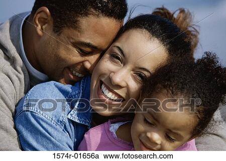 Stock Image - Close-up of parents hugging their daughter. Fotosearch