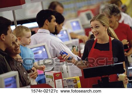 Stock Image - Customers standing at a checkout counter in a supermarket. Fotosearch