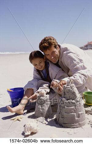 Stock Image - Father and his daughter making sand castles on the beach. Fotosearch