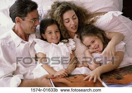 Stock Image - Father and mother lying in bed with their two daughters. Fotosearch