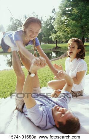 Stock Image - Father and mother playing with their daughter on a lawn. Fotosearch