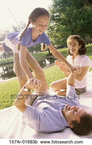 Stock Image - Father and mother playing with their daughter on a lawn. Fotosearch