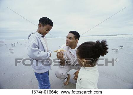 Father holding a starfish at the beach with his two children View Large Photo Image Stock Image - Father holding a starfish at the beach with his two children. Fotosearch