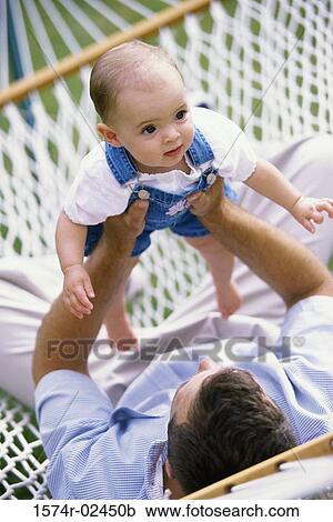 Stock Image - Father lying in a hammock playing with his baby boy. Fotosearch