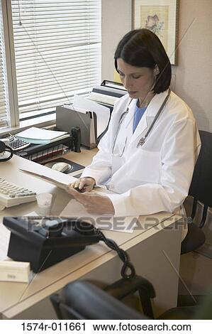 Stock Image - Female doctor sitting behind a desk at an office. Fotosearch