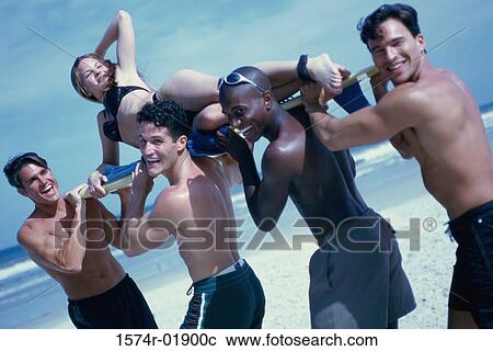 Stock Image - Four young men carrying a young woman on a surfboard. Fotosearch