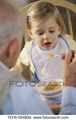 Stock Image - Grandfather feeding his granddaughter. Fotosearch