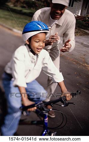 Stock Image - Grandfather helping his grandson ride a bicycle. Fotosearch