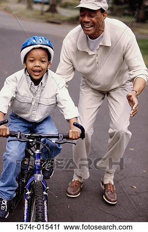Stock Image - Grandfather helping his grandson ride a bicycle. Fotosearch