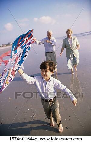 Stock Image - Grandson flying a kite at the beach with his grandparents. Fotosearch