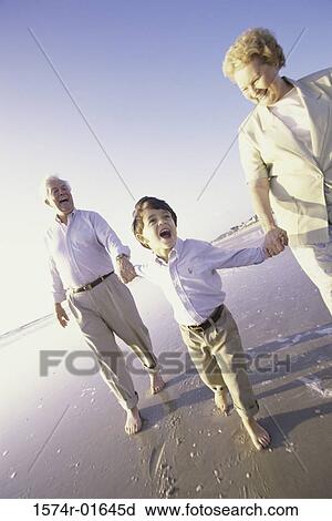 Stock Image - Grandson running at the beach with his grandparents. Fotosearch