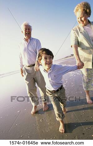 Stock Image - Grandson running at the beach with his grandparents. Fotosearch