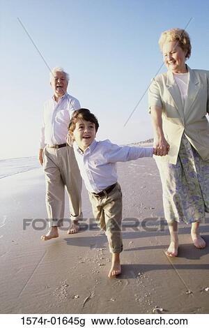 Stock Image - Grandson walking at the beach with his grandparents. Fotosearch