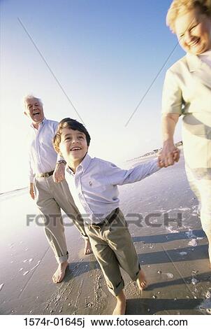 Stock Image - Grandson walking at the beach with his grandparents. Fotosearch