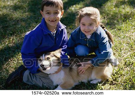 Stock Image - High angle view of a boy and a girl petting their dog. Fotosearch