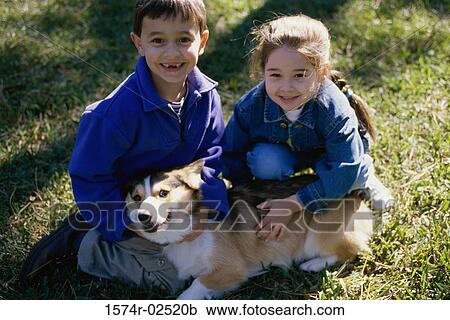 Stock Image - High angle view of a boy and a girl petting their dog. Fotosearch