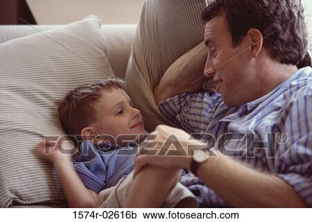 Stock Image - High angle view of a boy lying on a couch smiling with his father. Fotosearch
