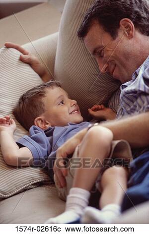High angle view of a boy lying on a couch smiling with his father View Large Photo Image Stock Image - High angle view of a boy lying on a couch smiling with his father. Fotosearch