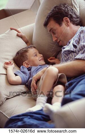 High angle view of a boy lying on a couch smiling with his father View Large Photo Image Stock Image - High angle view of a boy lying on a couch smiling with his father. Fotosearch