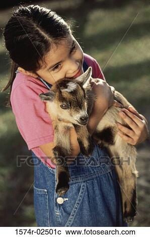 Stock Image - High angle view of a girl holding a kid goat in her arms. Fotosearch