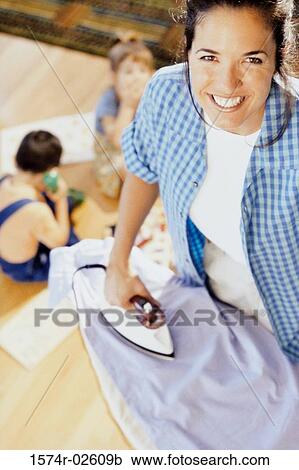 Stock Image - High angle view of a mother ironing clothes with her children playing nearby. Fotosearch