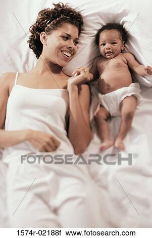Stock Image - High angle view of a mother lying on a bed with her baby boy. Fotosearch