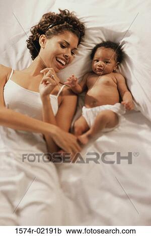 Stock Image - High angle view of a mother lying on a bed with her baby boy. Fotosearch