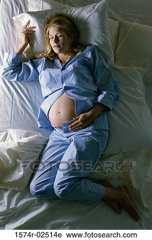 Stock Image - High angle view of a pregnant woman sleeping on a bed. Fotosearch