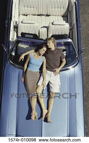Stock Photo - High angle view of a young couple lying on the hood of a convertible car. Fotosearch