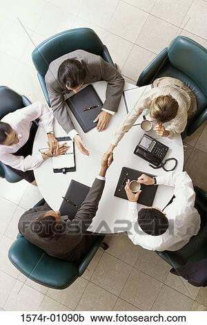Stock Image - High angle view of business executives shaking hands in a meeting. Fotosearch