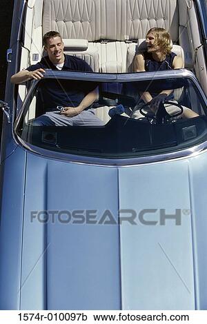 Stock Image - High angle view of two young men sitting in a convertible car. Fotosearch