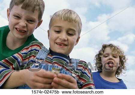 Low angle view of a boy standing with his friends holding a frog View Large Photo Image Stock Image - Low angle view of a boy standing with his friends holding a frog. Fotosearch