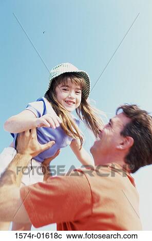 Stock Image - Low angle view of a daughter thrown up in the air by her father. Fotosearch