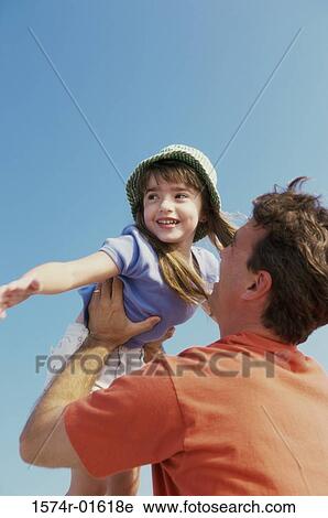 Stock Image - Low angle view of a daughter thrown up in the air by her father. Fotosearch