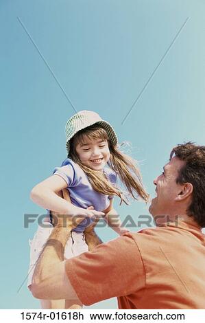 Stock Image - Low angle view of a daughter thrown up in the air by her father. Fotosearch