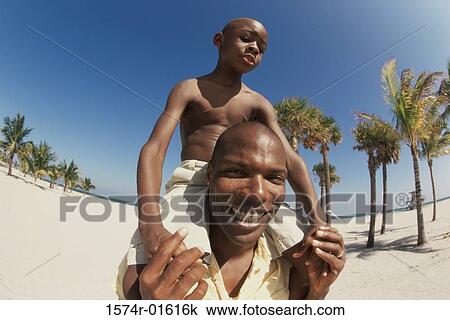 Stock Image - Low angle view of a father carrying his son on his shoulders. Fotosearch
