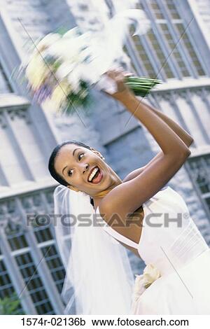 Stock Image - Low angle view of a newlywed young woman tossing the bouquet. Fotosearch