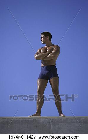 Low angle view of a young man standing with his arms folded View Large Photo Image Stock Photo - Low angle view of a young man standing with his arms folded. Fotosearch